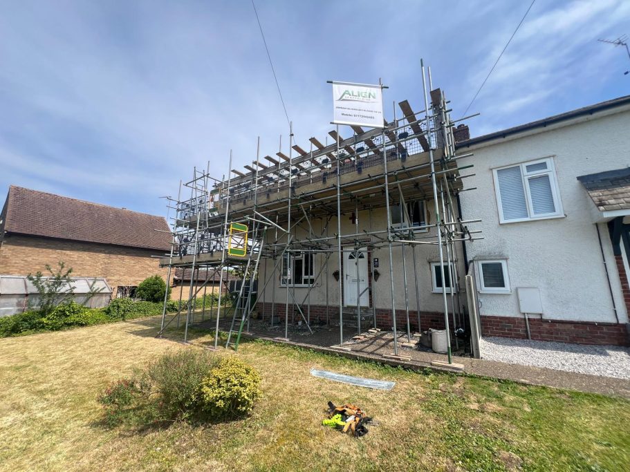 House under renovation with scaffolding in front, partially finished work, and clear sky.