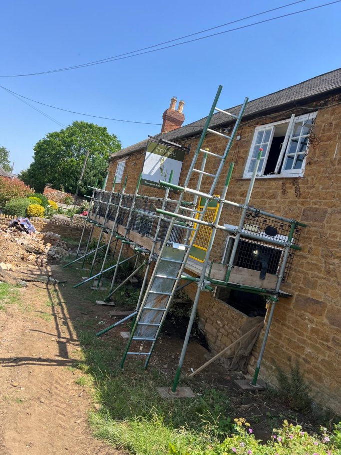 Scaffolding set up outside a brick house with an open window and clear blue sky.